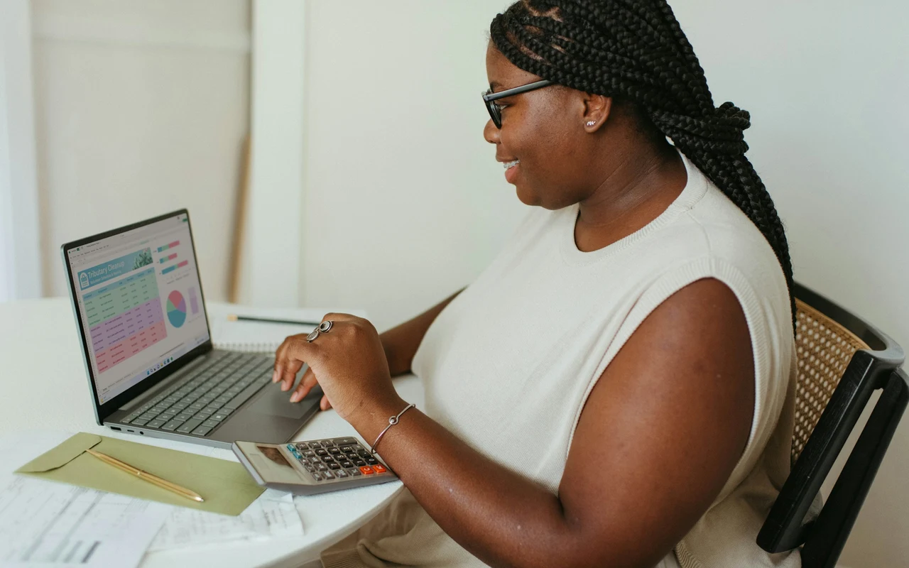 Profissional africana a analisar contas ao computador, com uma calculadora